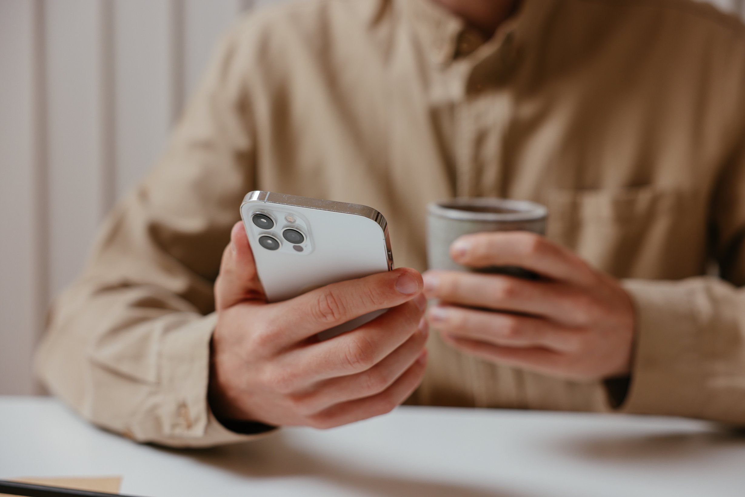 A Person in a Brown Long Sleeves Holding a iPhone And a Cup